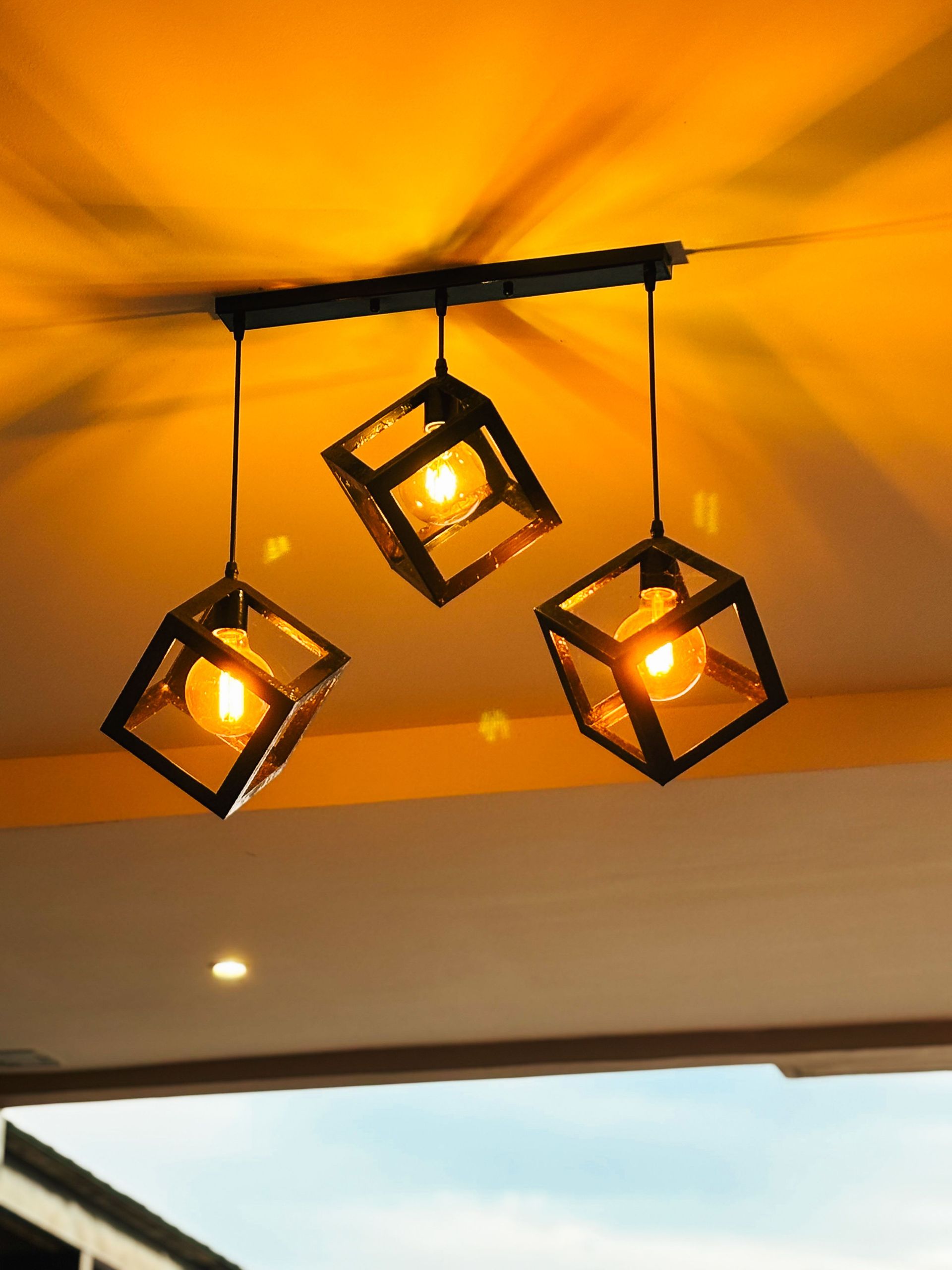 Artistic display of modern pendant lights with an industrial design against a vibrant yellow ceiling.